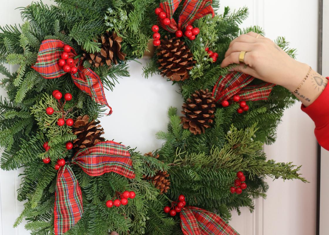 Woman holding evergreen Christmas wreath with red berries and bows