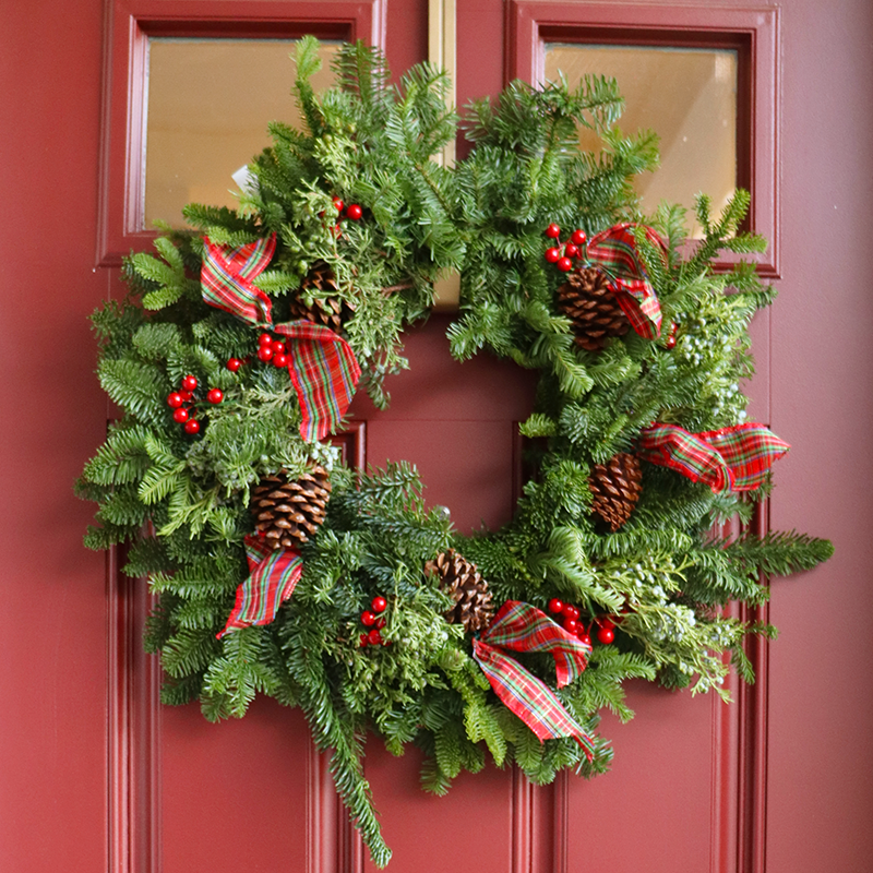Couronne de Noël fraîche avec des rubans rouges, des baies d'hiver et des pommes de pin sur une porte rouge