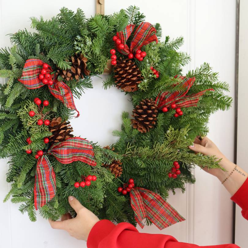 Couronne de Noël ornée de baies rouges, de rubans et de pommes de pin sur une porte blanche moderne