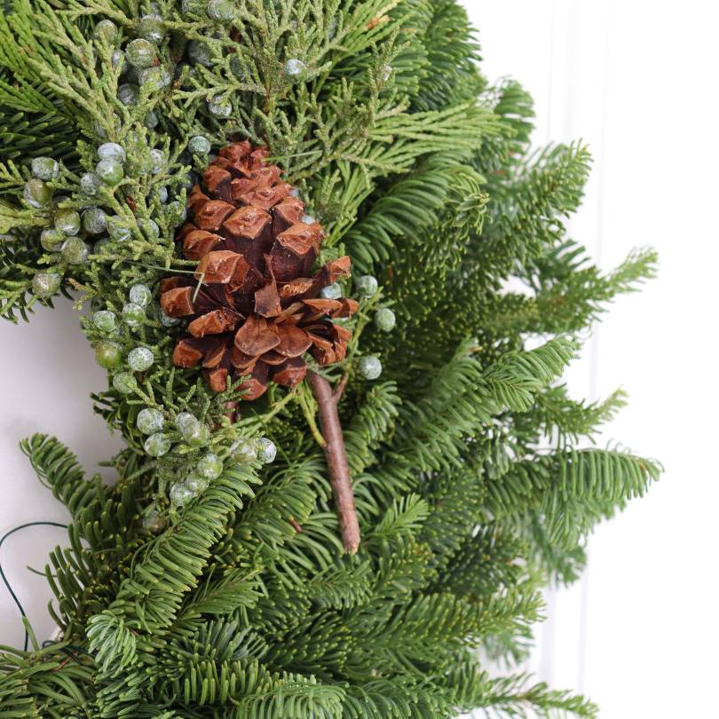Gros plan d'une couronne verte ornée de pommes de pin et de baies sur fond blanc
