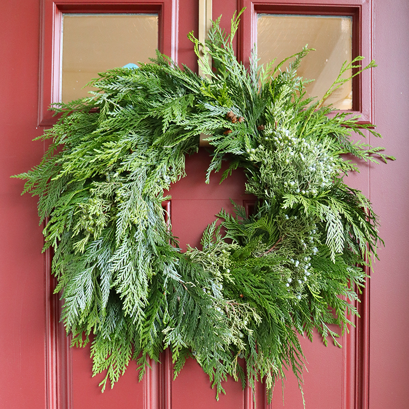 Couronne de Noël en cèdre vert et en genévrier sur une porte rouge