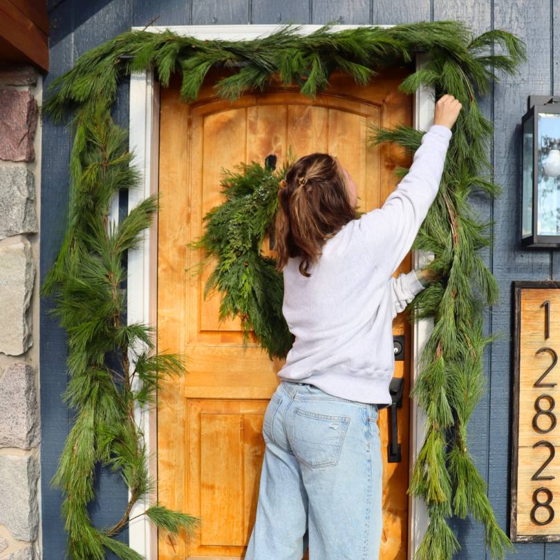 Une femme décore le porche d'entrée avec une guirlande de pin blanc frais.