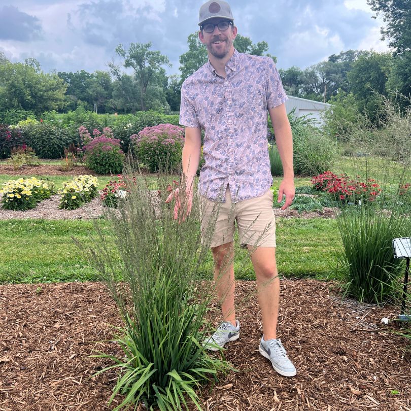 Man standing in a garden wearing a patterned shirt and sunglasses