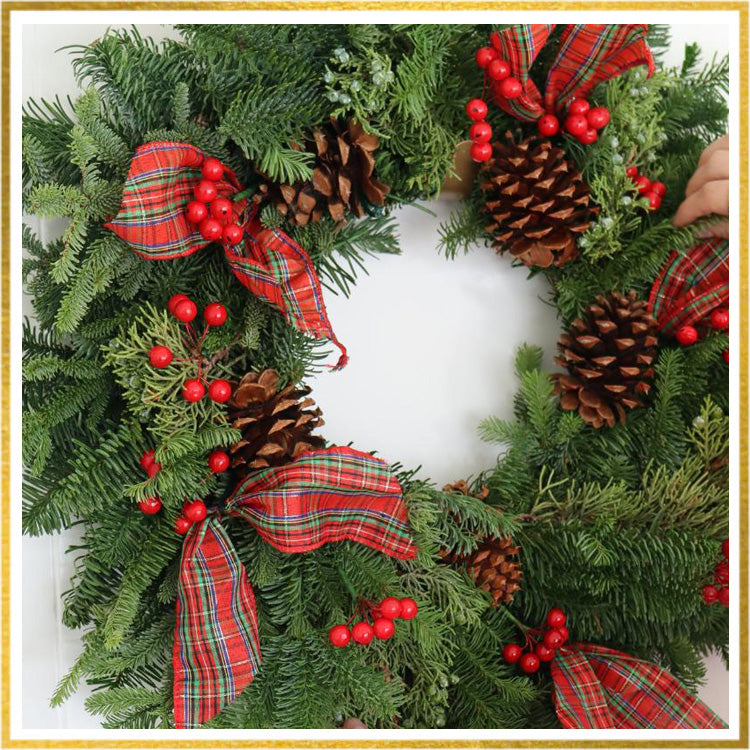 A close up of a wreath with red berries, pine cones, and bows